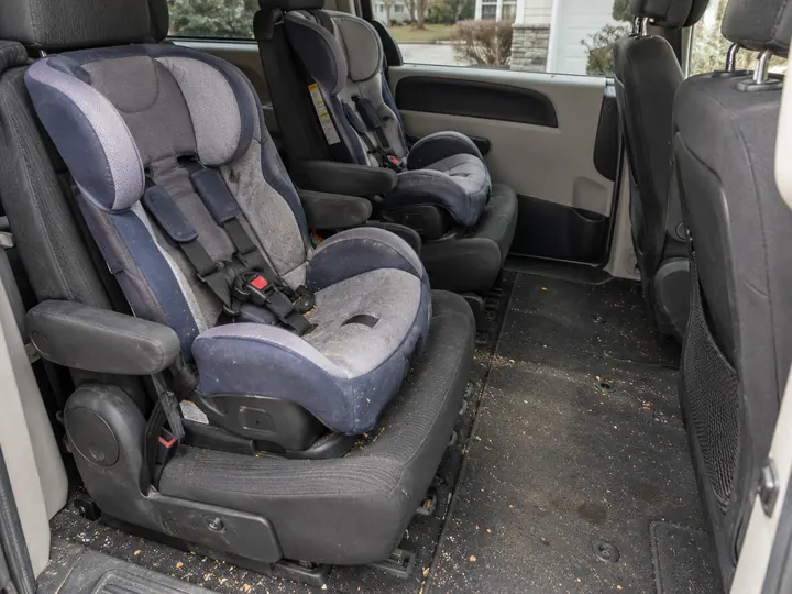 Illustration: back row of a family minivan with a child's car seat, crumbs and dirt across the floor, before the Reset